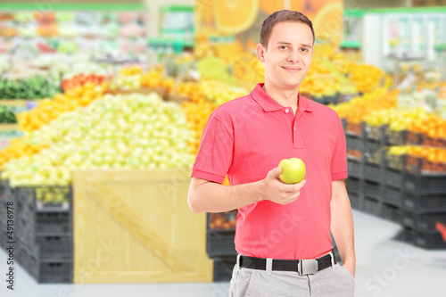 Photo: Man standing in a supermarket and holding an apple Man standing in a supermarket and holding an apple
