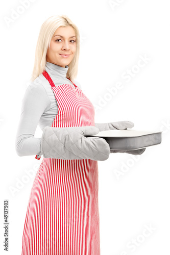 Photo: Young woman wearing cooking mittens and apron holding a baking t Young woman wearing cooking mittens and apron holding a baking t