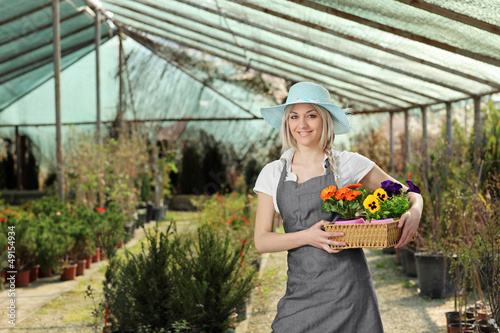 Photo: Female gardener posing with a basket full of flowes in a hothous Female gardener posing with a basket full of flowes in a hothous