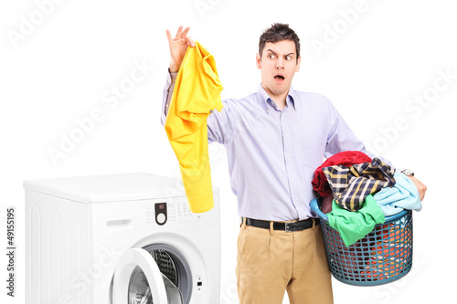 Photo: Young man standing next to a washing machine and holding dirty l Young man standing next to a washing machine and holding dirty l