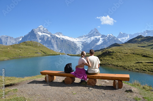 Photo: Travelers on a bench enjoying Alpine panorama Travelers on a bench enjoying Alpine panorama