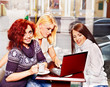 Women at laptop drinking coffee in a cafe.