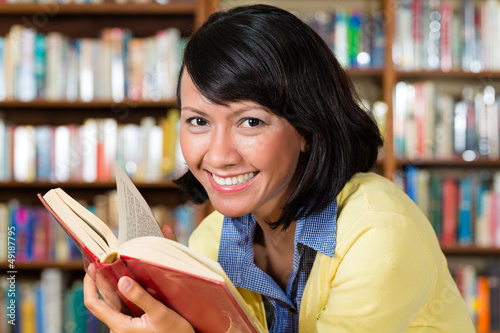 Photo: Asian girl in library reading a book Asian girl in library reading a book