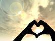 Conceptual heart shape human hand silhouette over sky at sunset