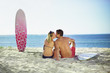 A loving couple sitting on the beach kissing with their surfboar