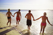 Two couples wearing swimwear and running into the ocean - rearvi
