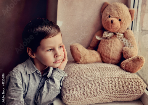 Photo: little boy with a toy on a knitted pillow looking out the window little boy with a toy on a knitted pillow looking out the window