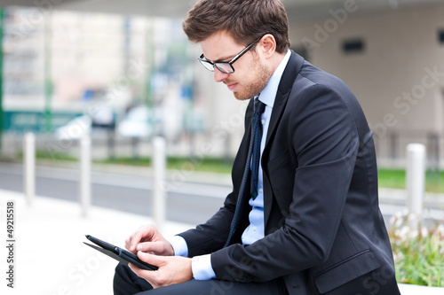 Photo: Young businessman using a tablet on a bench in the city Young businessman using a tablet on a bench in the city