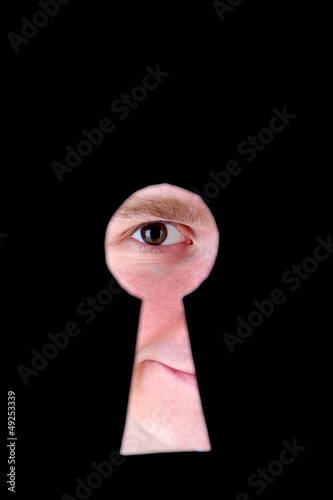 Photo: Man eye looking through hole in keyhole, on black background Man eye looking through hole in keyhole, on black background