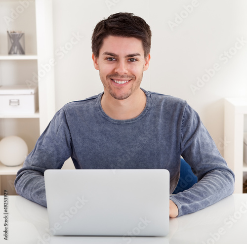 Photo: Smiling young man using a laptop Smiling young man using a laptop