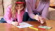 Mother with daughter sit on sofa at wooden table and draw with