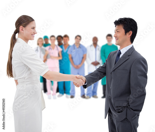 Photo: Business people shaking hands with medical staff in background Business people shaking hands with medical staff in background
