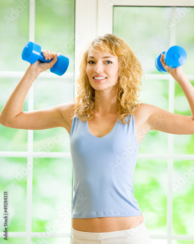 Photo: Young smiling woman with dumbbells, indoors Young smiling woman with dumbbells, indoors