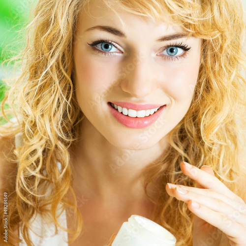 Photo: Happy smiling woman applying creme, indoor Happy smiling woman applying creme, indoor