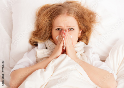 Photo: ill sick young woman sneezes into a handkerchief in bed ill sick young woman sneezes into a handkerchief in bed