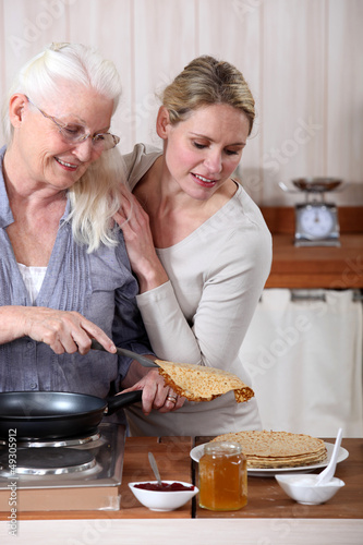 Photo: A mature mother and her adult daughter making crepes. A mature mother and her adult daughter making crepes.
