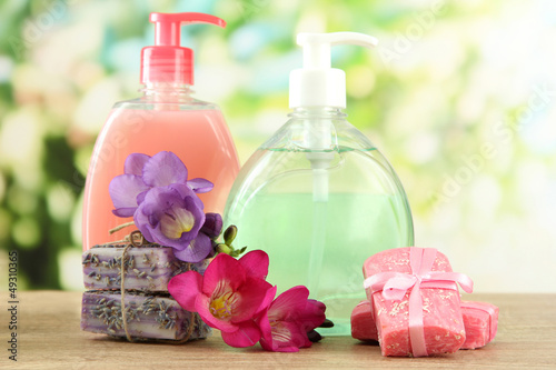 Photo: Liquid and hand-made soaps on wooden table, on green background Liquid and hand-made soaps on wooden table, on green background