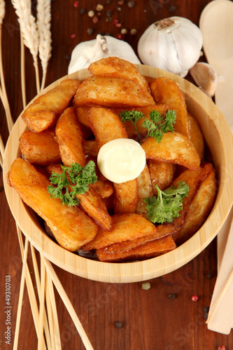 Photo: Appetizing village potatoes in bowl on wooden table close-up Appetizing village potatoes in bowl on wooden table close-up