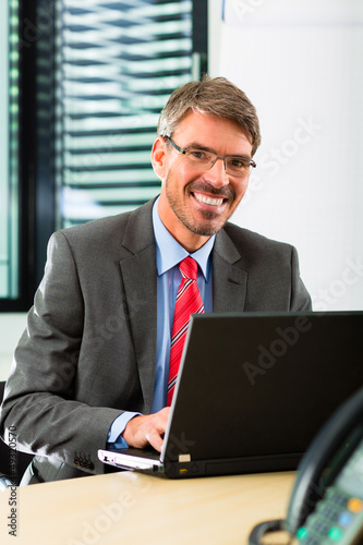 Photo: businessperson with laptop in his business office businessperson with laptop in his business office