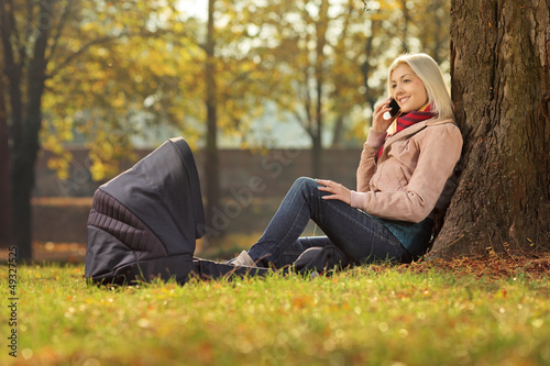Photo: Young mother sitting in a park with her baby in a carrycot and t Young mother sitting in a park with her baby in a carrycot and t
