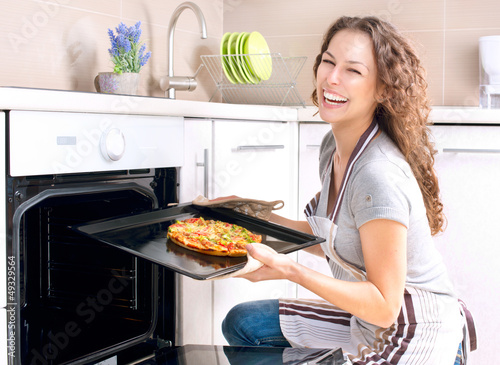 Photo: Happy Young Woman Cooking Pizza at Home Happy Young Woman Cooking Pizza at Home