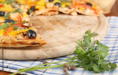 Photo: Tasty pizza with kitchen herbs on wooden table close-up Tasty pizza with kitchen herbs on wooden table close-up