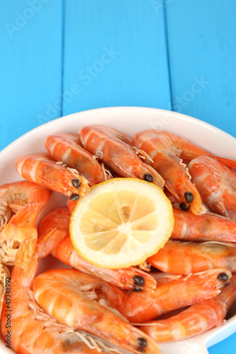 Photo: Shrimps with lemon on plate on wooden table close-up Shrimps with lemon on plate on wooden table close-up