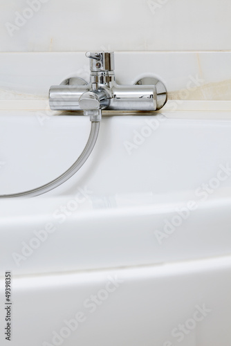 Photo: Modern metal faucet on white ceramic bathtub, interior detail Modern metal faucet on white ceramic bathtub, interior detail