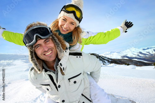Photo: Cheerful snowboarder holding girlfriend on his back Cheerful snowboarder holding girlfriend on his back