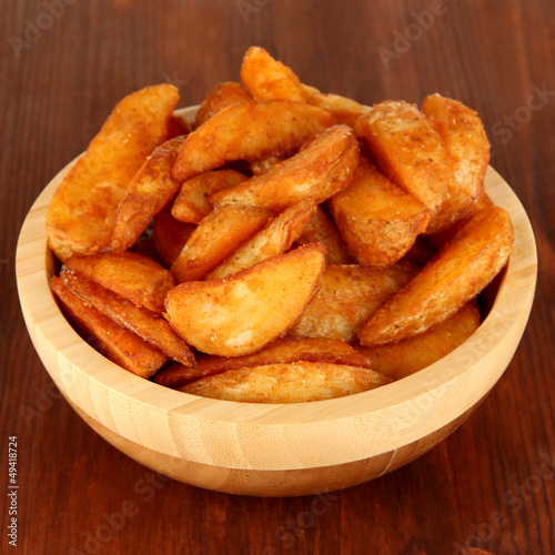 Photo: Appetizing village potatoes in bowl on wooden table close-up Appetizing village potatoes in bowl on wooden table close-up