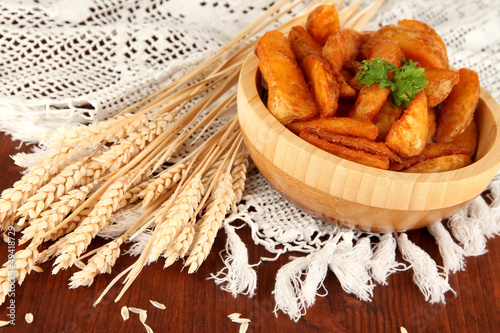Photo: Appetizing village potatoes in bowl on wooden table close-up Appetizing village potatoes in bowl on wooden table close-up