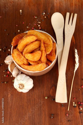 Photo: Appetizing village potatoes in bowl on wooden table close-up Appetizing village potatoes in bowl on wooden table close-up
