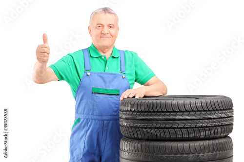 Photo: A mature worker posing on car tires and giving thumb up A mature worker posing on car tires and giving thumb up