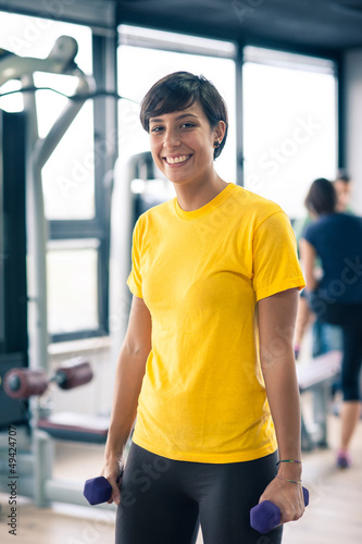 Photo: Young girl exercising with dumbbells in the gym. Young girl exercising with dumbbells in the gym.