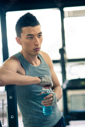 Photo: Young asian man having a rest drinking a beverage in the gym. Young asian man having a rest drinking a beverage in the gym.