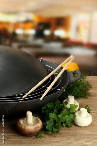 Photo: Black wok pan and vegetables on kitchen wooden table, close up Black wok pan and vegetables on kitchen wooden table, close up