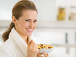 Portrait of happy young woman in bathrobe eating breakfast 