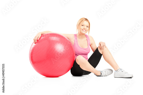 Photo: A young female athlete sitting on a floor next to a pilates ball A young female athlete sitting on a floor next to a pilates ball