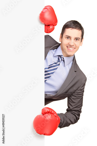 Photo: Young smiling businessman wearing boxing gloves and posing behin Young smiling businessman wearing boxing gloves and posing behin