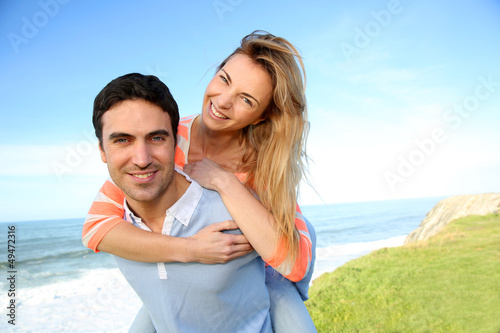 Photo: Man giving piggyback ride to girlfriend by the sea Man giving piggyback ride to girlfriend by the sea