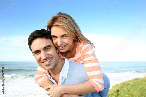 Photo: Man giving piggyback ride to girlfriend by the sea Man giving piggyback ride to girlfriend by the sea