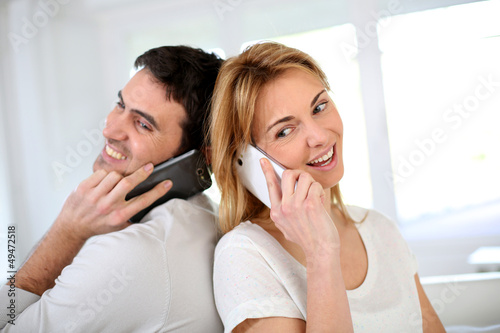 Photo: Couple using smartphone, sitting back to back Couple using smartphone, sitting back to back