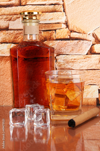 Photo: Bottle and Glass of whiskey and cigar on brick wall background Bottle and Glass of whiskey and cigar on brick wall background