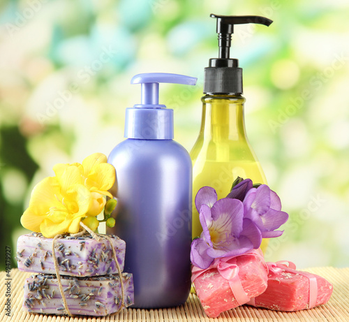 Photo: Liquid and hand-made soaps on wooden table, on green background Liquid and hand-made soaps on wooden table, on green background