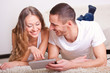 couple lying on carpet and looking at tablet