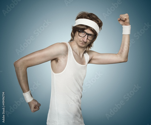 Photo: Funny retro nerd flexing his muscle over blue background Funny retro nerd flexing his muscle over blue background