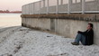 Sad woman sitting against a seawall long shot