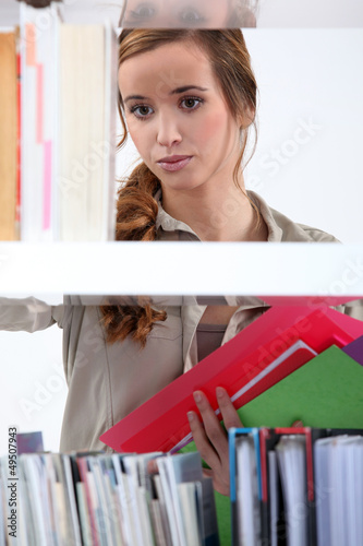 Photo: Woman putting books back on shelf. Woman putting books back on shelf.