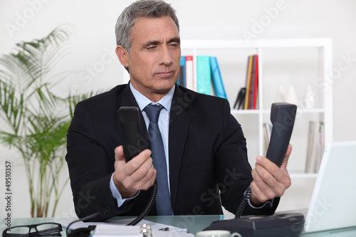 Photo: Over worked businessman holding two telephones Over worked businessman holding two telephones