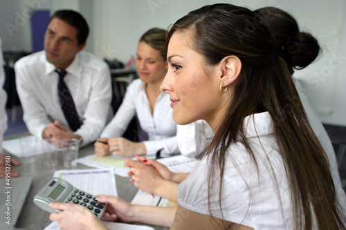 Photo: Woman using a calculator at an office team meeting Woman using a calculator at an office team meeting